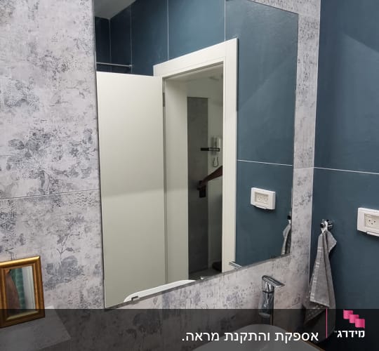 מראה מלבנית תלויה על קיר בחדר אמבטיה